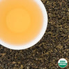 Pale-amber cup of Ana’s Organic First Flush Nepali green tea on loose leaves, USDA Organic seal