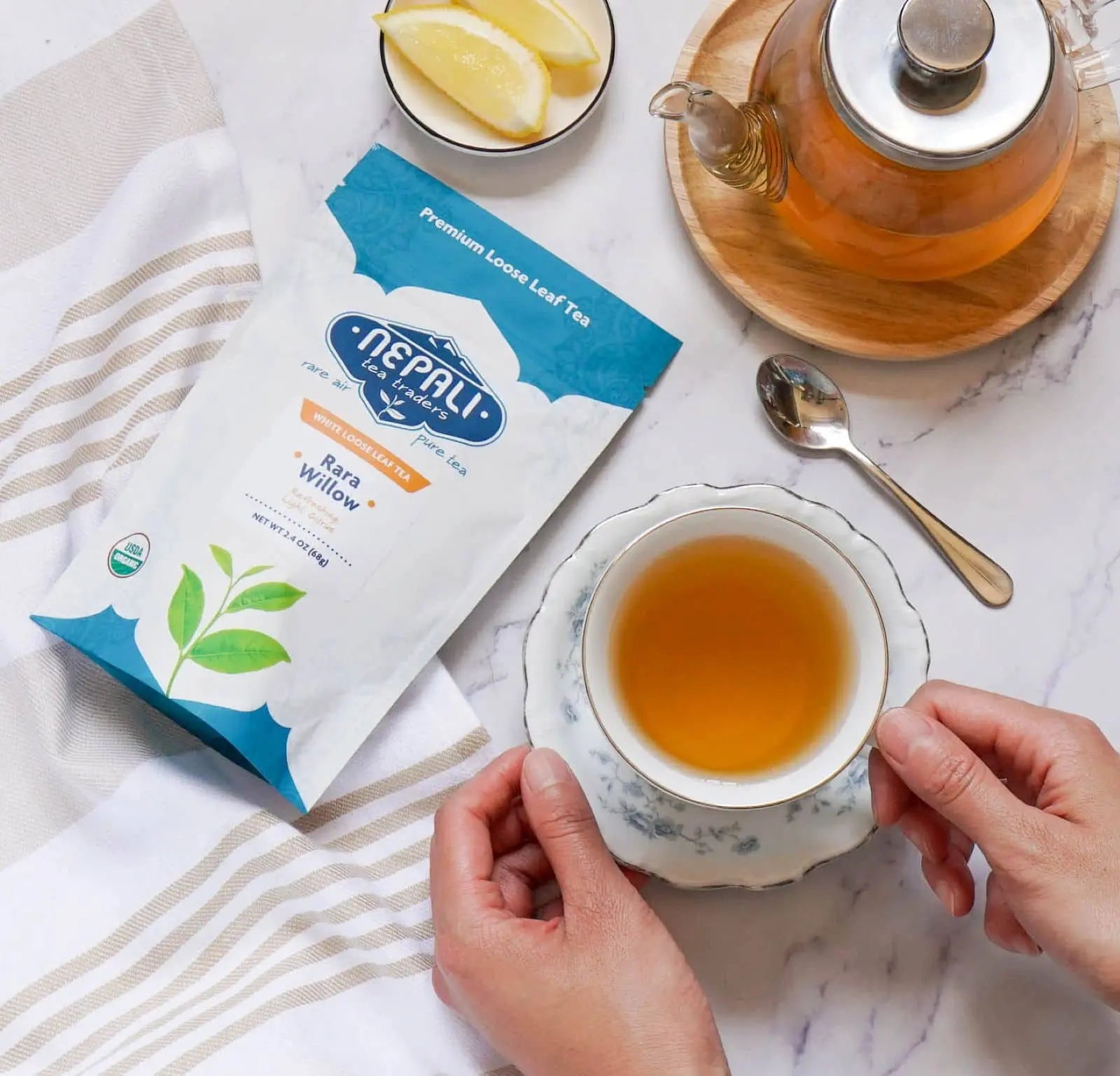 Rara Willow Organic White Tea from Nepal—Nepali Tea Traders pouch with a brewed teacup, glass teapot, and lemon slices.