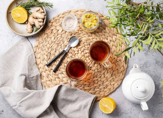 Two cups of tea with teapot on woven mat, lemon and ginger at the side—clean intermittent fasting concept