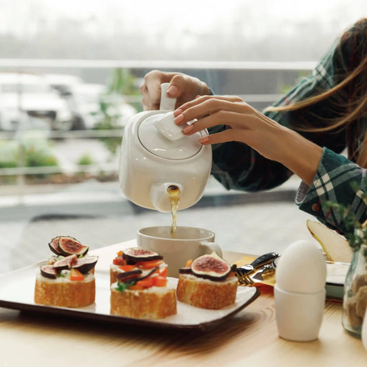 Hand pouring Nepali black tea from a white teapot into a cup at breakfast