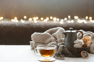 Cozy glass cup of hot tea with teapot and blanket for a warm winter tea ritual.