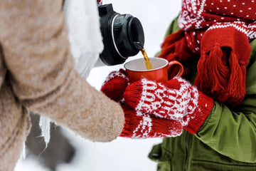 Pouring hot tea from a thermos into a red mug on a snowy day (best tea for cold weather).