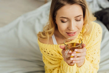 Woman in cozy yellow sweater sipping soothing tea for bloating and gut comfort