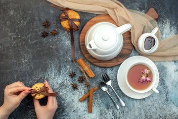 Overhead of a white teapot and a cup of black Nepali tea with rose buds, cinnamon and star anise on slate—relaxing tea ritual for energy and focus.