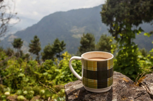 Cup of tea on a stone ledge overlooking green hills and the Himalayan mountains in Nepal.
