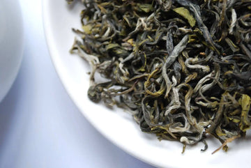 Close-up of hand-rolled Nepali green tea leaves on a white plate