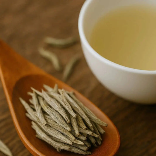 Wooden spoon filled with silver needle tea leaves beside a white teacup of golden brewed tea