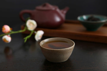 A cup of Nepali loose leaf tea in a handcrafted ceramic bowl with a clay teapot and flowers in the background