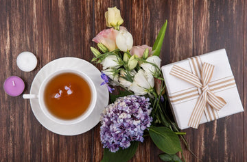 Cup of Nepali black tea with wrapped gift box and flowers on wooden table
