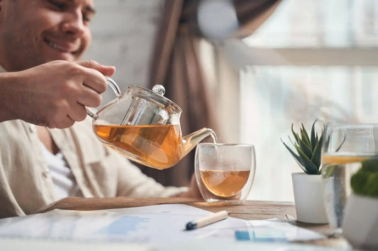 Man pouring brewed loose leaf tea from a glass teapot into a clear cup