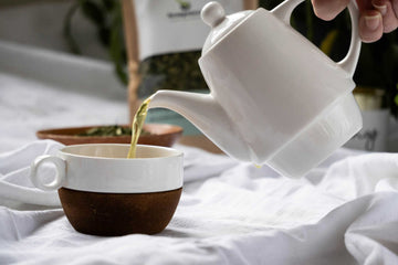 Close-up of Nepali green tea being poured into a ceramic cup from a white teapot