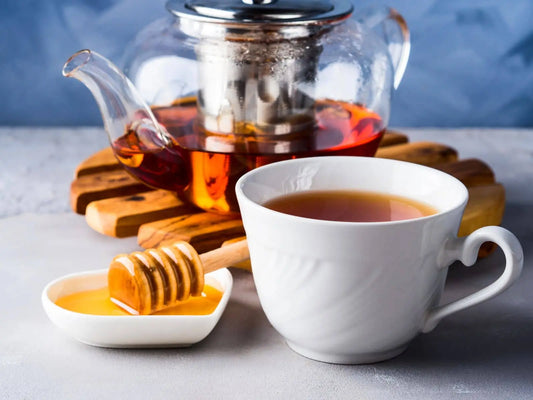 A glass teapot of black tea and a honey dipper, showing how to sweeten robust black tea blends.