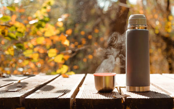 Steaming thermos tea on a wooden table in cool weather