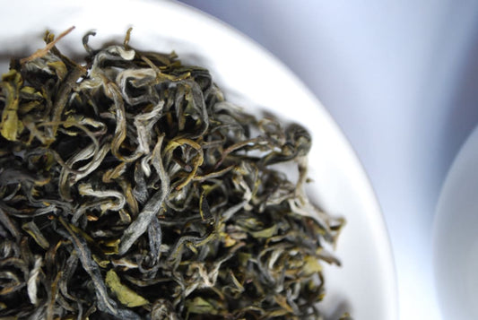 Steeping organic green tea in a glass teapot with whole loose leaves.