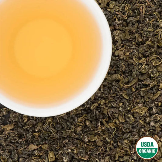 Pale-amber cup of Ana’s Organic First Flush Nepali green tea on loose leaves, USDA Organic seal

