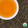 Pale-amber cup of Pokhara Classic organic Nepali green tea on loose leaves, USDA Organic seal