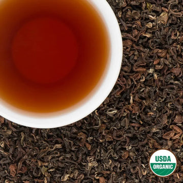Top-down view of brewed Dragon Claw Oolong tea in a white cup on loose-leaf Nepali oolong tea, with USDA Organic badge