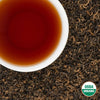White cup of brewed Himalayan Golden Organic Black Tea on loose leaves with USDA Organic seal