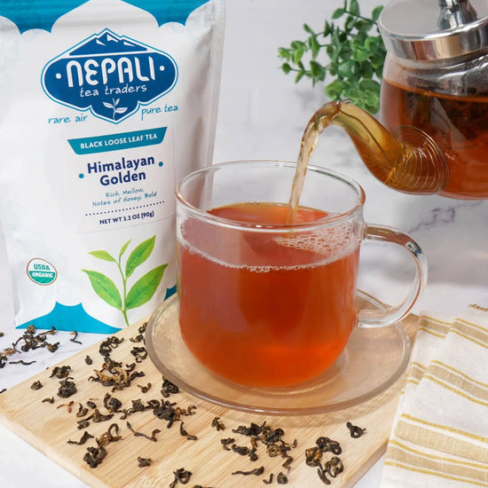 Himalayan Golden organic loose-leaf black tea from Nepal poured into a glass mug beside a Nepali Tea Traders pouch