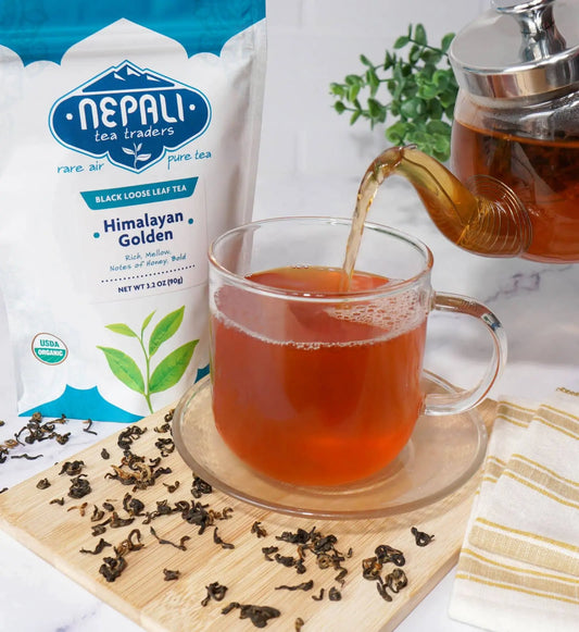 Himalayan Golden organic loose-leaf black tea from Nepal poured into a glass mug beside a Nepali Tea Traders pouch