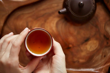 Hand holding a cup of rich amber Nepali black tea on a wooden tea tray