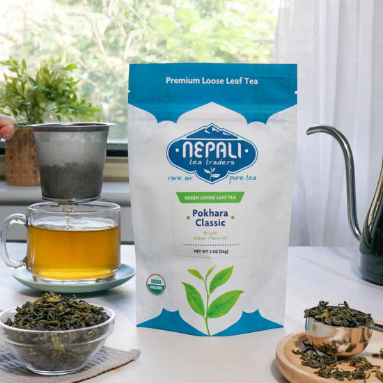 Pokhara Classic Organic Green Tea from Nepal—Nepali Tea Traders pouch with brewed green tea, loose leaves, and a strainer over a glass mug.