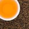 A white cup of brewed Sagarmatha Gold black tea showing a vibrant honey-colored liquor next to dry loose leaves.