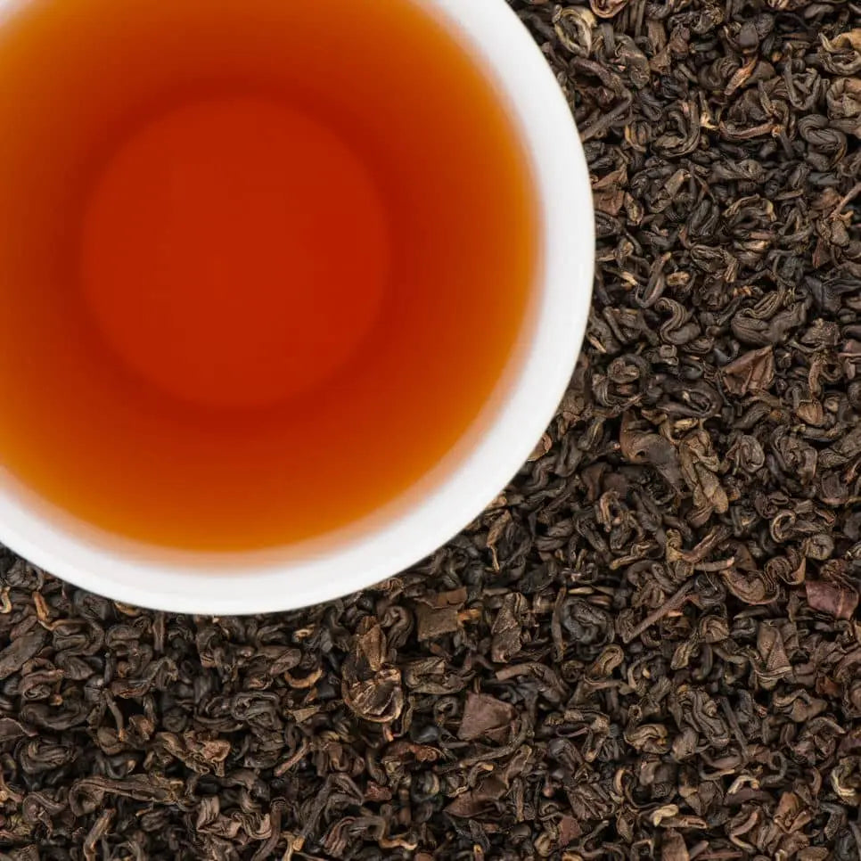 A cup of deep amber smoked oolong tea from Nepal with dark, tightly curled loose leaves.