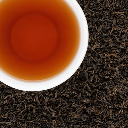 Amber liquor of Snow Leopard black tea in a white cup over loose leaves