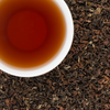 Golden Nepali Dragon Claw Oolong Tea in cup with loose leaf background